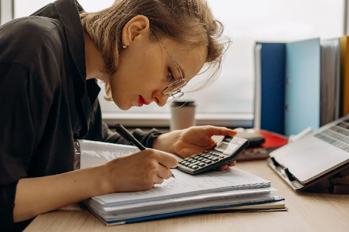 Bookkeeper manually entering transactions from paper records with a calculator